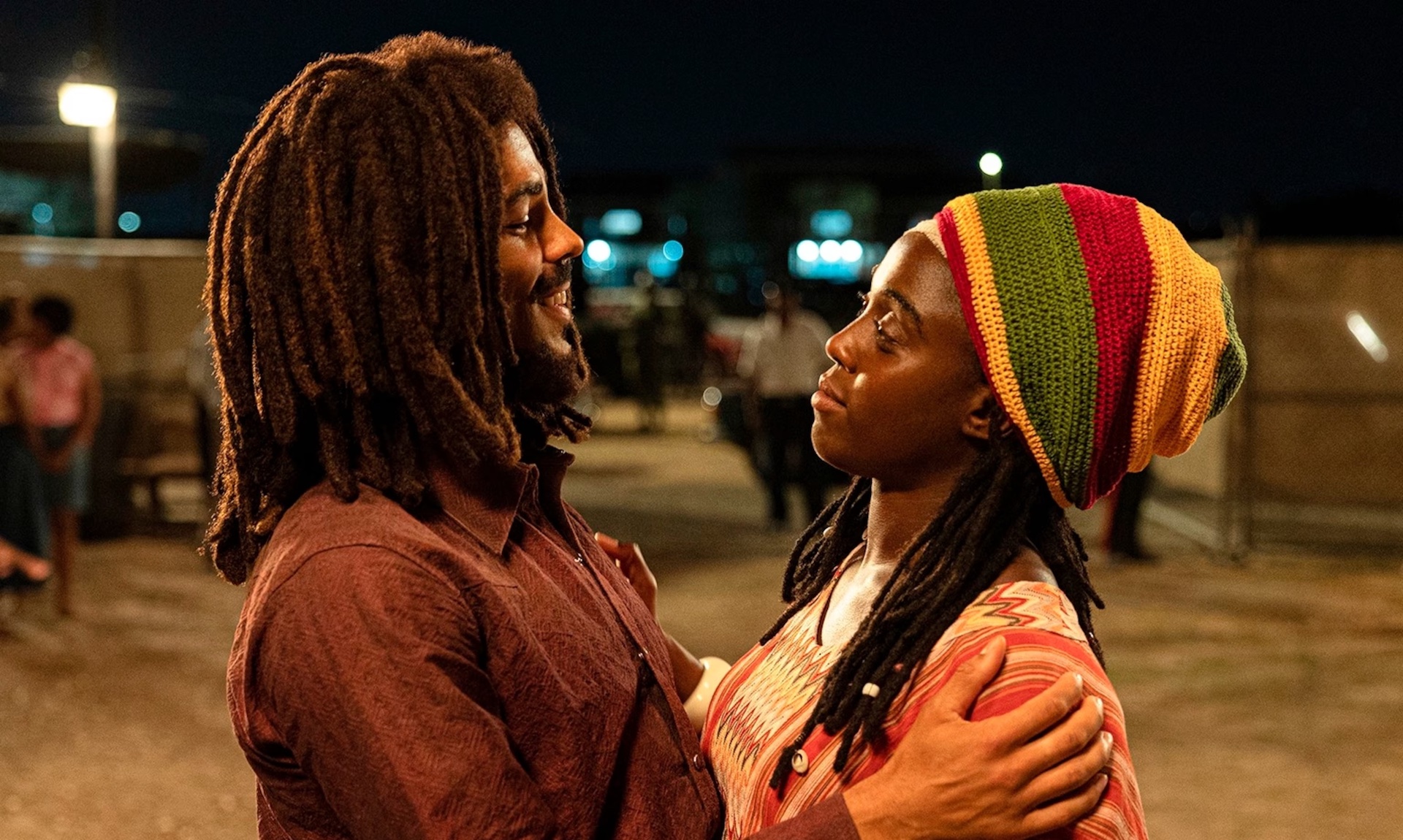 Bob Marley (Kingsley Ben-Adir) and Rita Marley (Lashana Lynch) hugging in a parking lot in 'Bob Marley: One Love' 