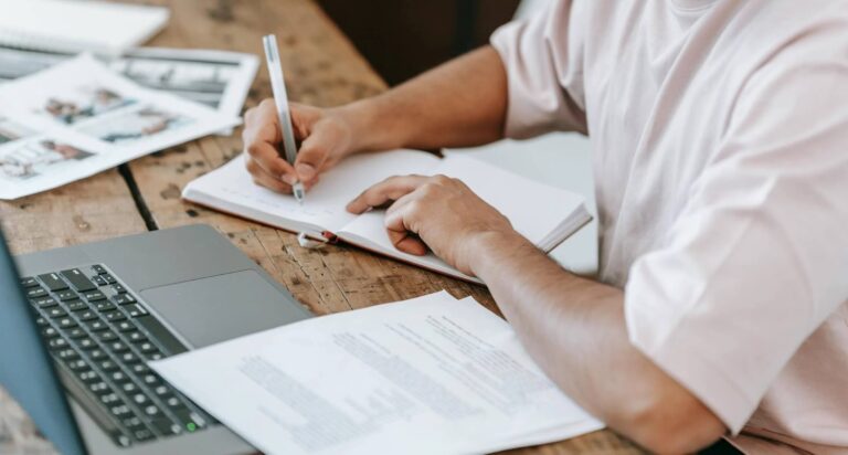 A person is a white shirt writing into a notebook; Writers' Room Etiquette for Screenwriters