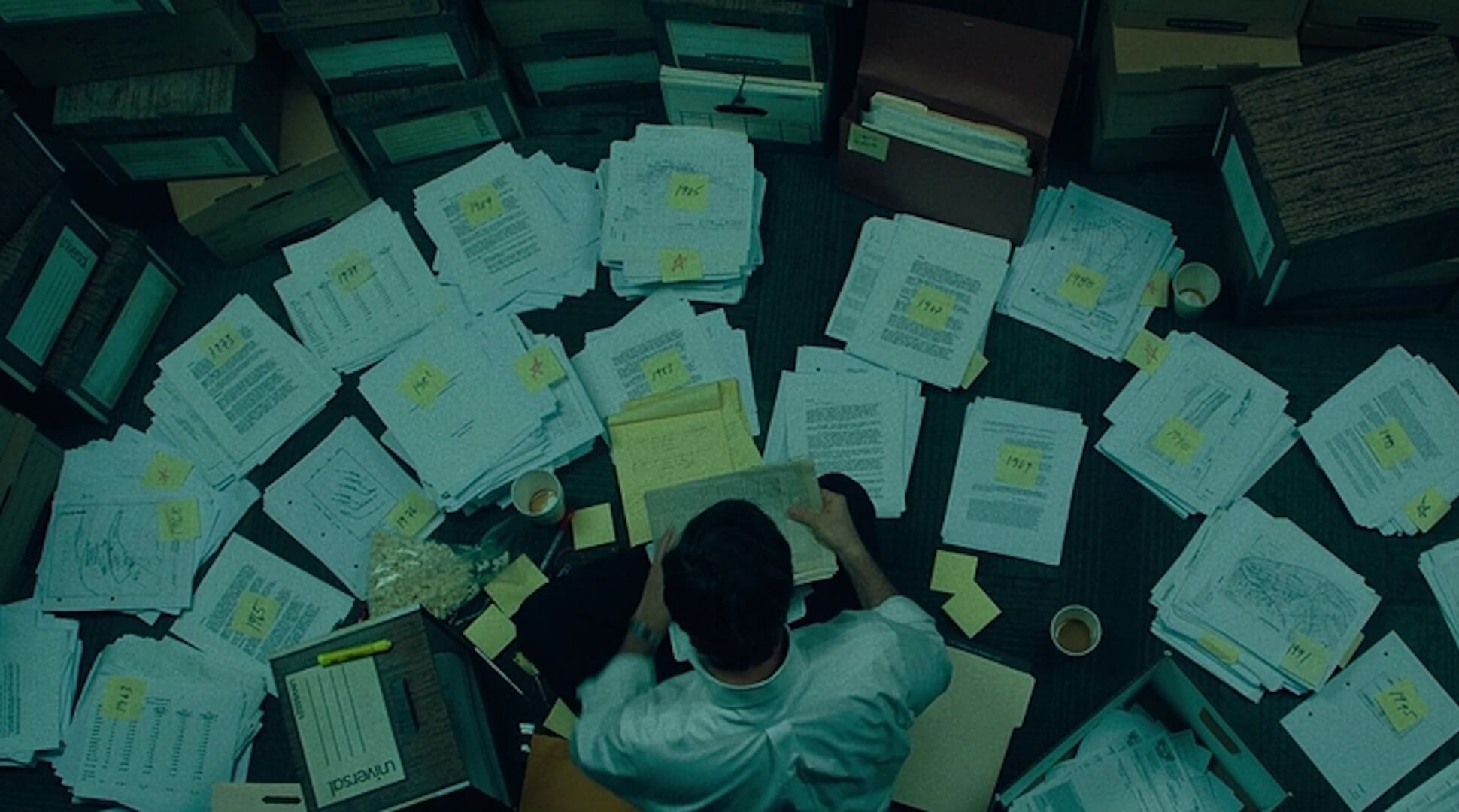 An overhead shot looking at a man's back as he organizes files into piles in 'Dark Waters,' The Power of Organization in Screenwriting