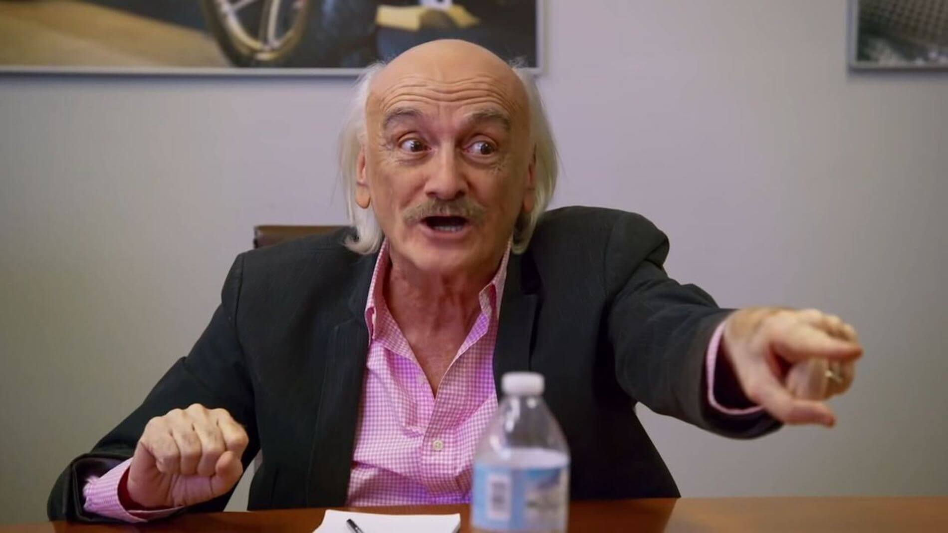 An older man in a pink dress shirt and black jacket points across a table in a skit for 'I Think You Should Leave'