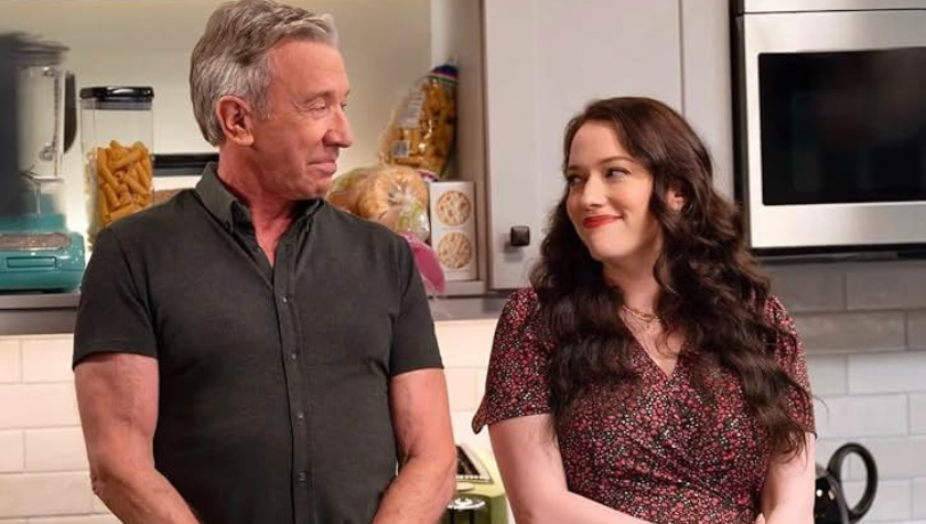 Tim Allen and Kat Dennings stand in the kitchen, looking at each other affectionately. Pasta, bread, and crackers stacked on a shelf in the background in Shifting Gears
