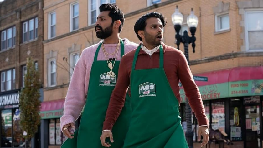 Image from 'Deli Boys' of two Pakistani-American brothers standing shocked in the middle of the street. They are wearing 2 green deli aprons